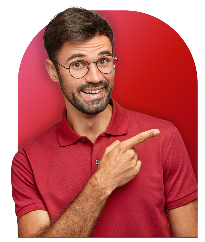 Indoor Shot Of Positive Bearded Male In Casual Red T Shirt Points With Index Finger Aside - SPE Soluções